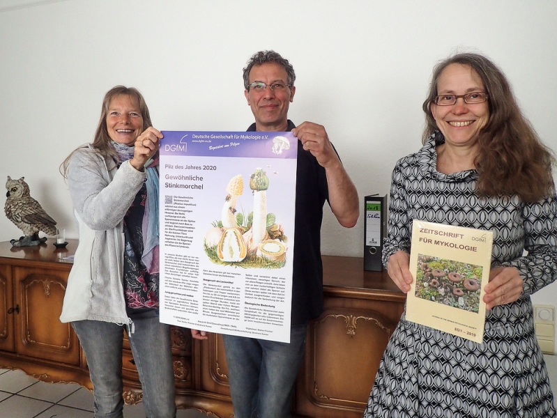 Rita Lüder (links) und El Bekkay Berchid, der Geschäftsführer von „Der Natur-Shop“, mit dem Poster über den Pilz des Jahres 2020, und seine Mitarbeiterin Ina Lüdecke (rechts) mit einem Heft der Zeitschrift für Mykologie.